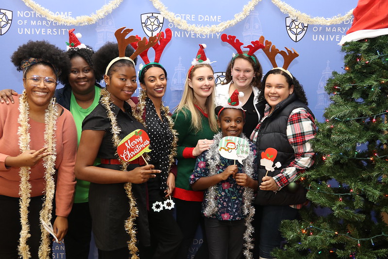 Group photo of female students wearing reindeer headbands next to a Christmas tree