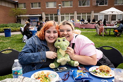 two students hold toy gator near table