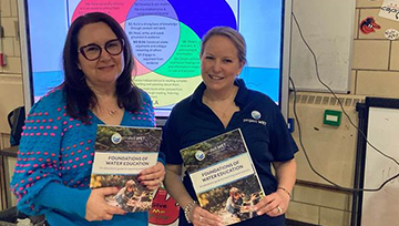 Lisa Pallett and Juliann Dupuis stand next to each other in a classroom, while each holding a book