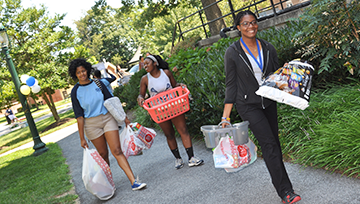 3 students carrying their belongings to move into the residence hall