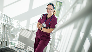 Student in scrubs leaning against a stair railing
