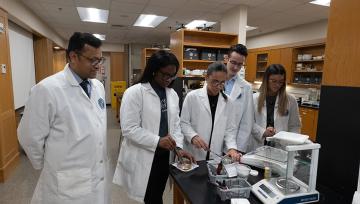 Students and a professor wearing white lab coats work in a lab