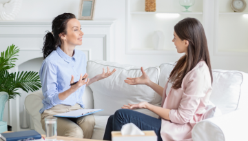 Two women talking to each other while sitting on a sofa