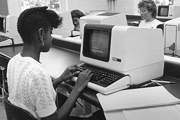 Black & white photo of students in a computer lab with old computers