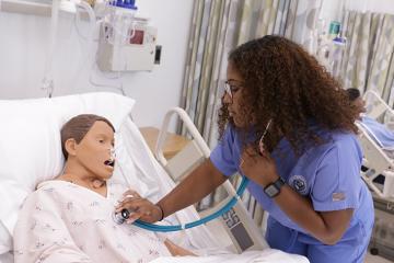 Female wearing blue nursing scrubs checks temperature on mannikin in a nursing simulation lab