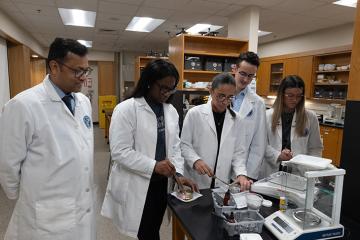 Students and a professor wearing white lab coats work in a lab