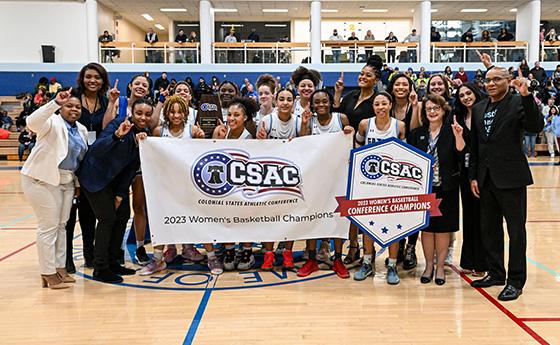 Women's basketball team, coaches, and administrators pose with championship banner