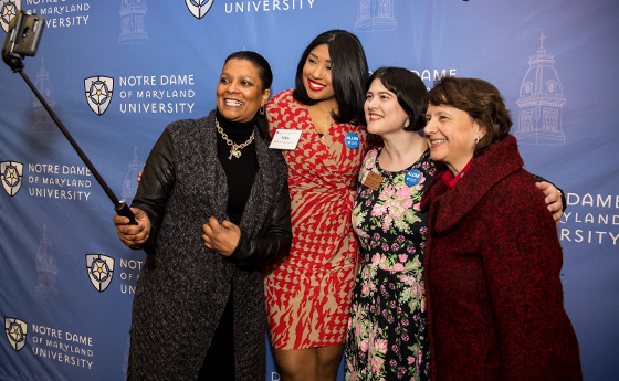 Four women taking a selfie in front of the NDMU step and repeat