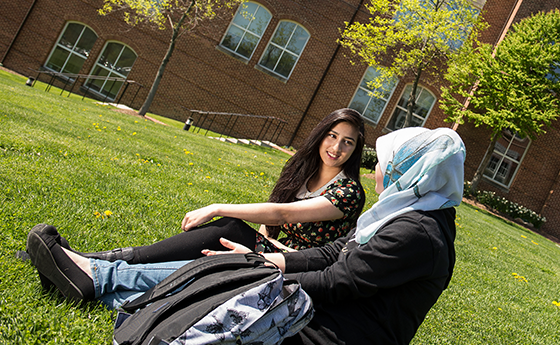Two students sitting on the lawn having a conversation
