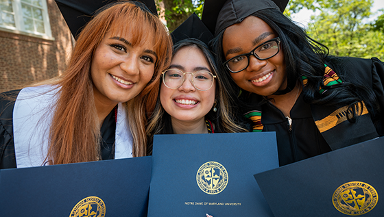 three students in caps and gowns smiling and holding diplomas