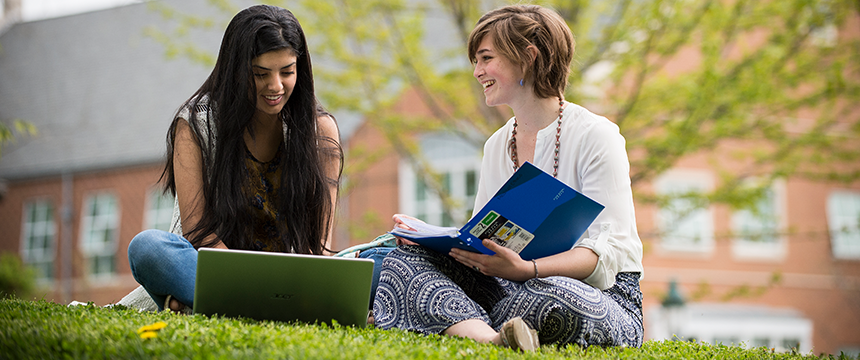 Two girls sitting in the grass looking at books and smiling
