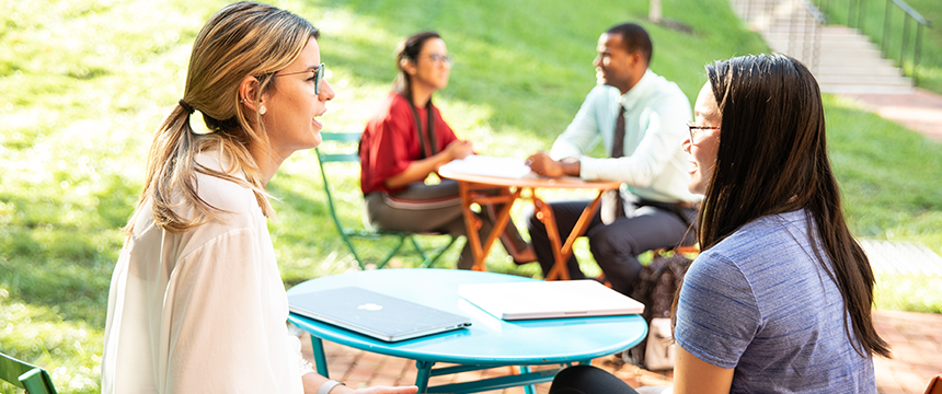 4 Students sitting at cafe tables on campus