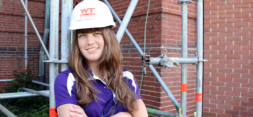 Student wearing a hard hat with scaffolding behind her