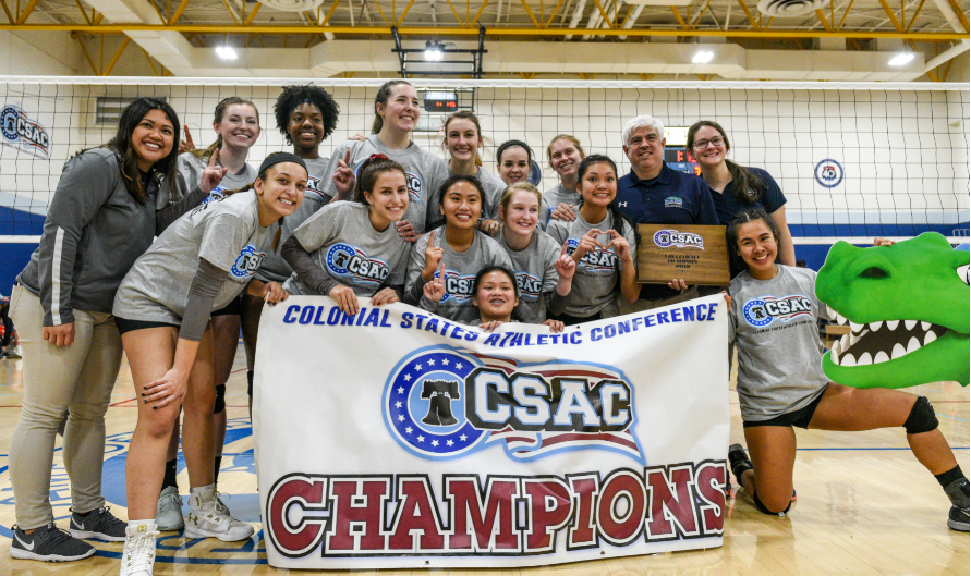 The volleyball team and coaches pose with the CSAC Champions banner.